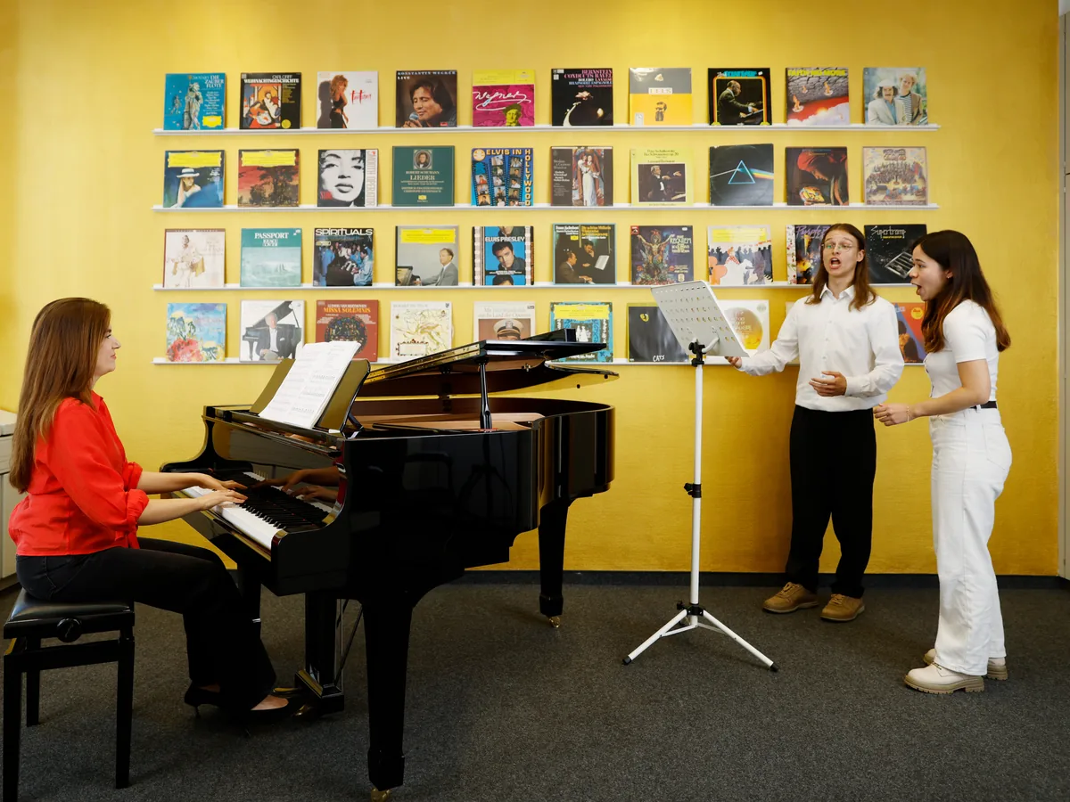 Unterrichtsraum von Migenas Musikschule in Düsseldorf: Migena begleitet am Flügel ein Gesangsduett am Notenständer